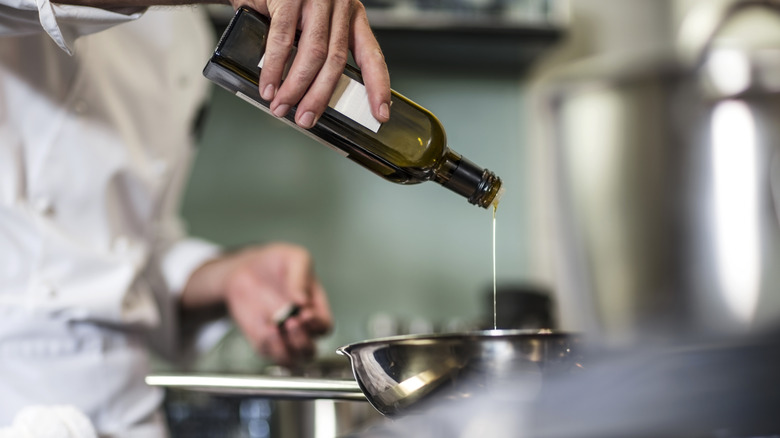 A chef pouring oil into a pot.