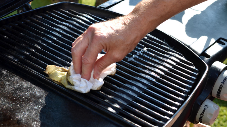 A person oiling grill grates using a paper towel.