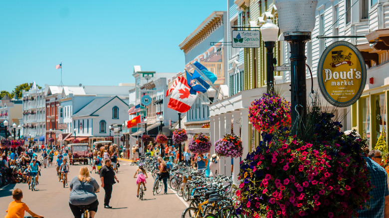 Road on Mackinac Island with people cycling, shops on the right hand side, including Doug's Market line the street.