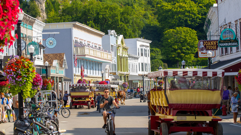 Main road on Mackinac Island with stores and shops on either side and people riding bicycles and carts on the street.