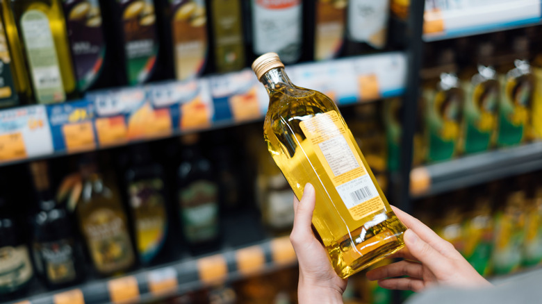 A close up of hands holding a bottle of olive oil in the grocery store