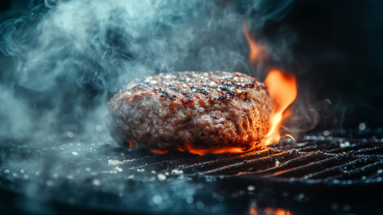 A thick burger patty sizzling on a flaming grill