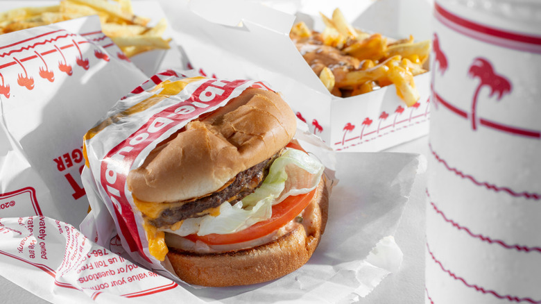 Close up of a wrapped burger next to fries and a soda