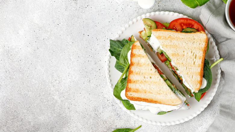 Wooden board with sliced bread and mayo and tomato covered bread