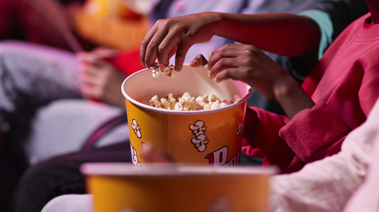 People reach into a bucket of popcorn in a movie theater