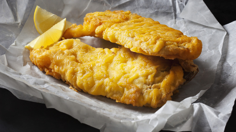 Two pieces of fried fish with lemon slices on parchment paper.