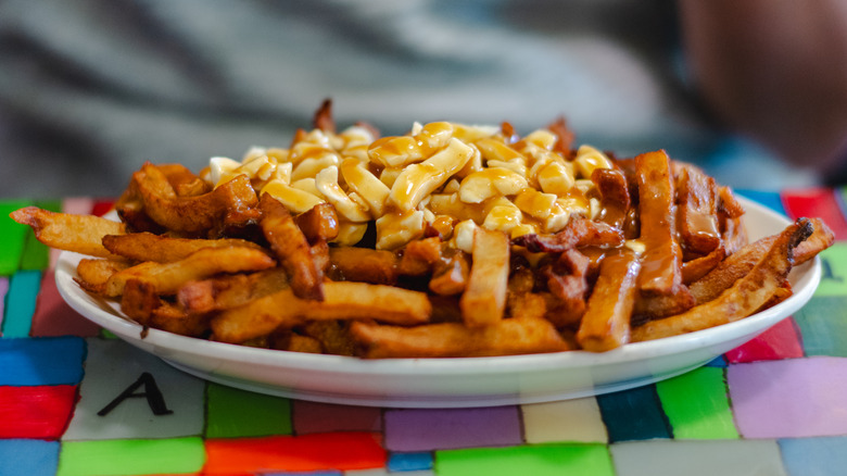 Plate of poutine on a colorful cloth with a blurred person on the background.