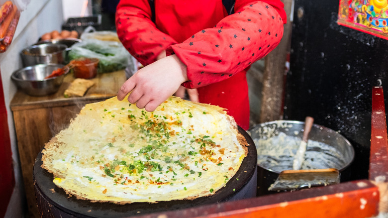 Person in red cooking Chinese jianbing on griddle