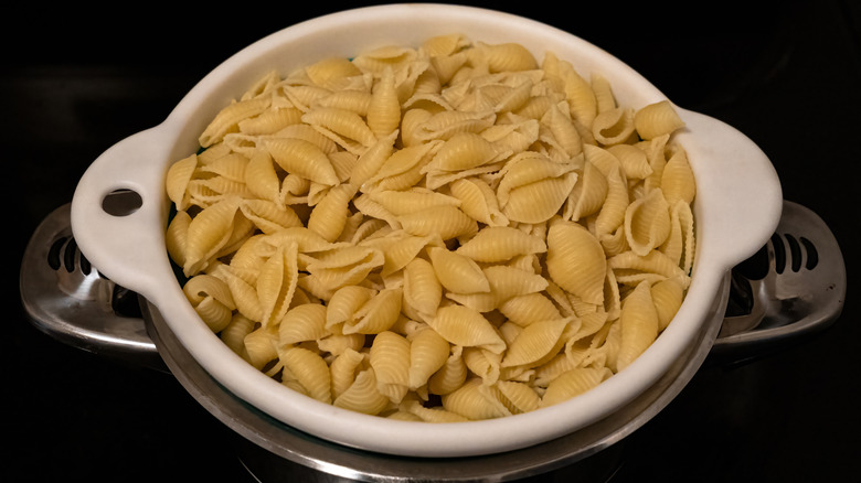 A colander filled with pasta shells sits over a metal pot