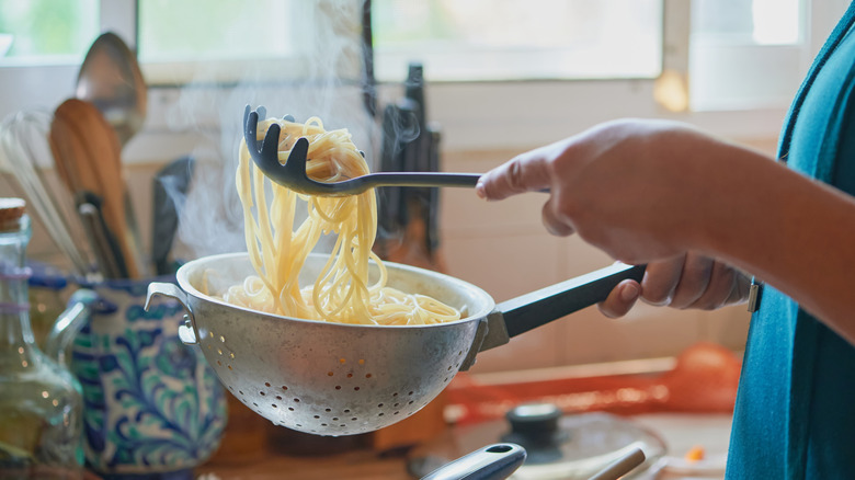 A person holding a pasta strainer and slotted spoon over a sink