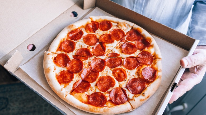 A person holding a pepperoni pizza in a box.