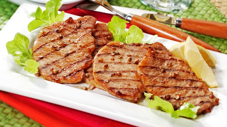 Plate of thin pork chop with a bed of lettuce and two lemon slices