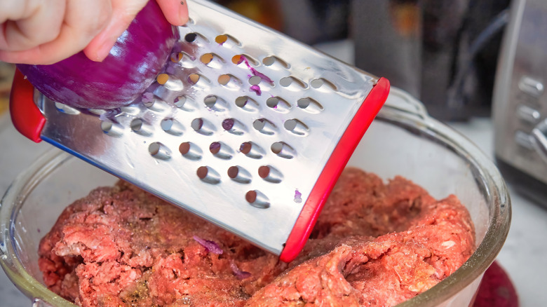 A person grating red onion into ground beef.