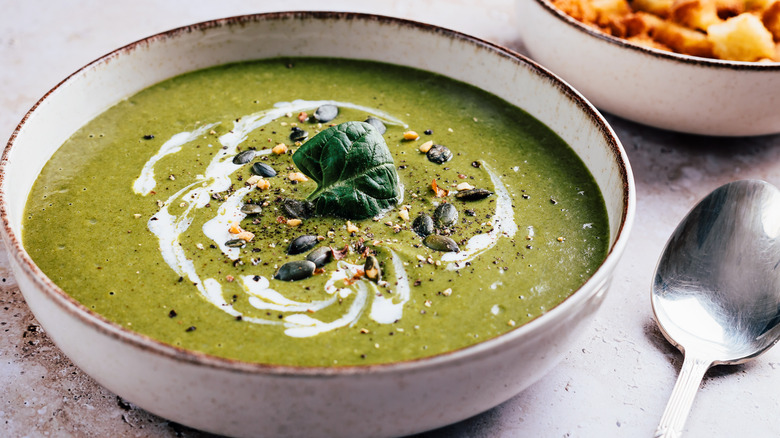 Creamy green soup with sour cream and various seeds as garnish.