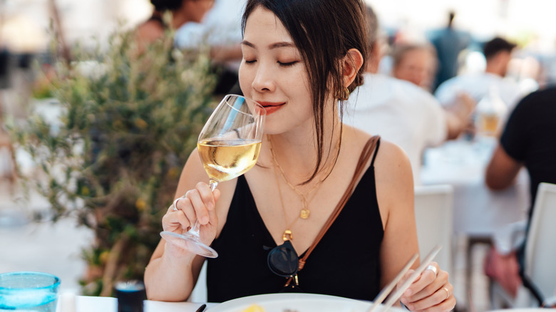 A woman smelling a glass of white wine at a restaurant