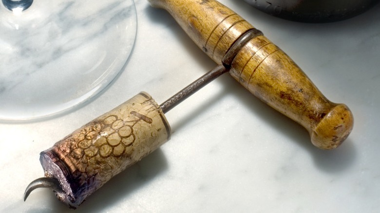 Wine cork and wine key on white marble table next to wine glass and wine bottle.