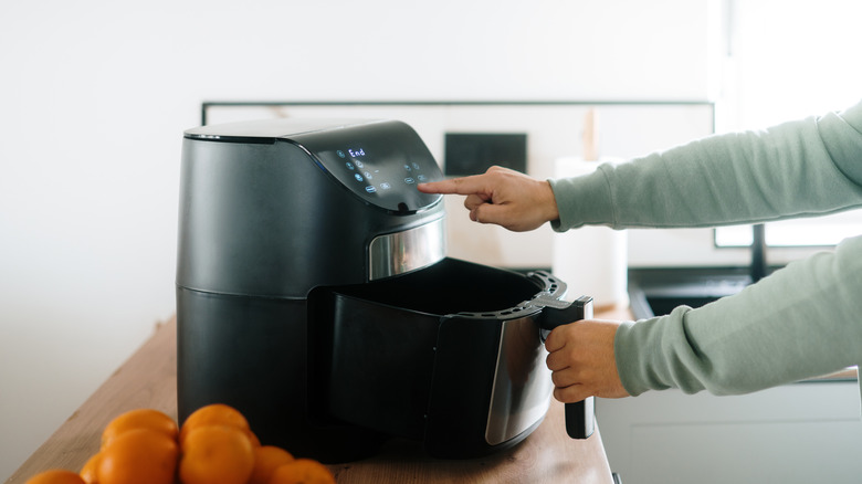 a hand pushing in the basket of an air fryer while the other hand pushes a button