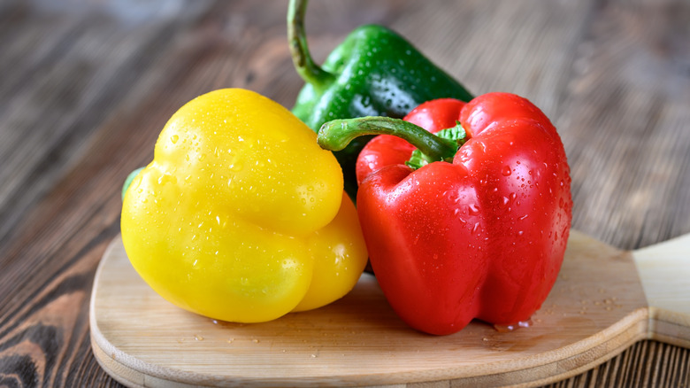 Three wet bell peppers sitting on a cutting board