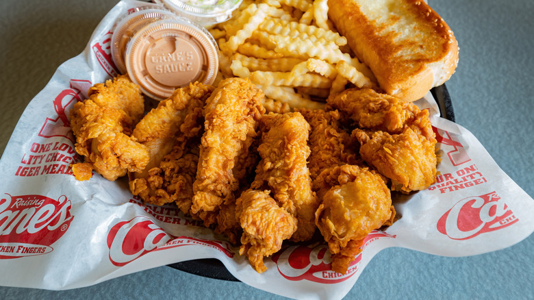 A basket of Raising Cane chicken fingers with fries, toast, and sauce containers