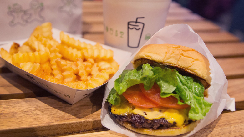 A Shake Shack burger with fries and a drink in the background