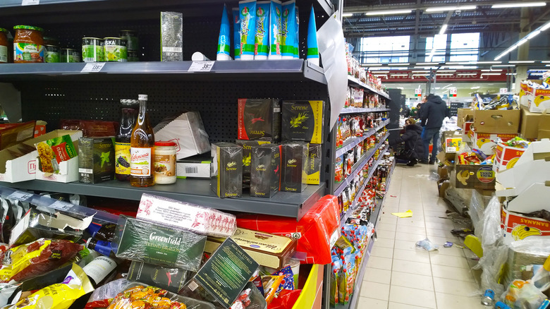 A dirty grocery store aisle with various disheveled products and debris on the floor