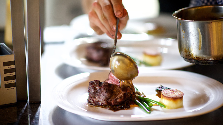 A chef pours sauce over a fancy cut of steak