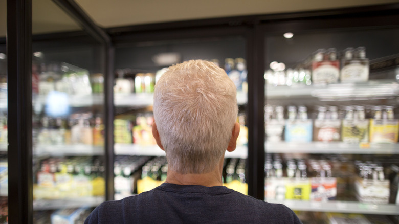 man standing in front of beer cooler at store