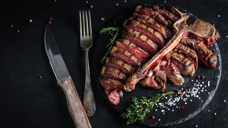 T-bone steak served on a black slate with thyme and salt.