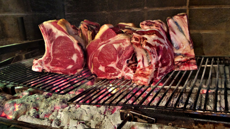 Thick steaks cooking on a grill over hot coals.