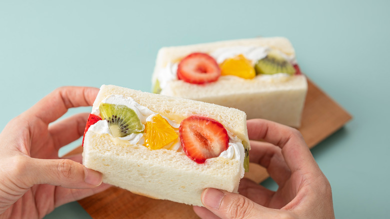 Hands hold a Japanese sando sandwich with colorful fruit.