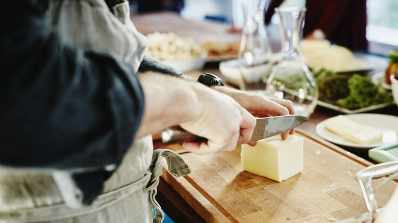 Chef cutting cold butter with a knife on a cutting board