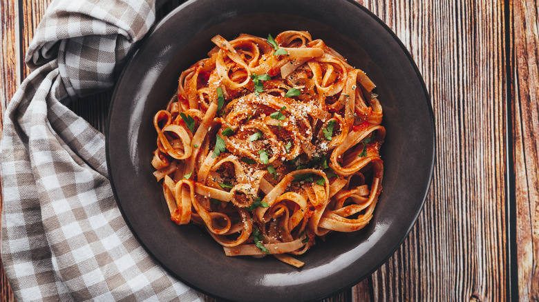 Tagliatelle pasta coated with tomato sauce in a black dish on a wooden table