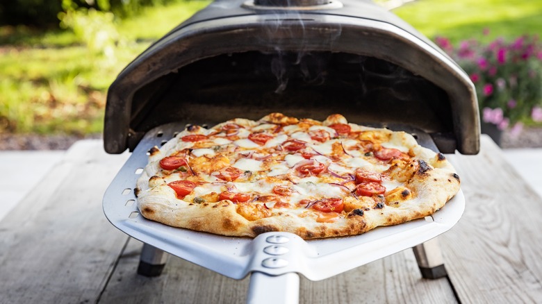 a freshly baked pizza being pulled out of an outdoor pizza oven