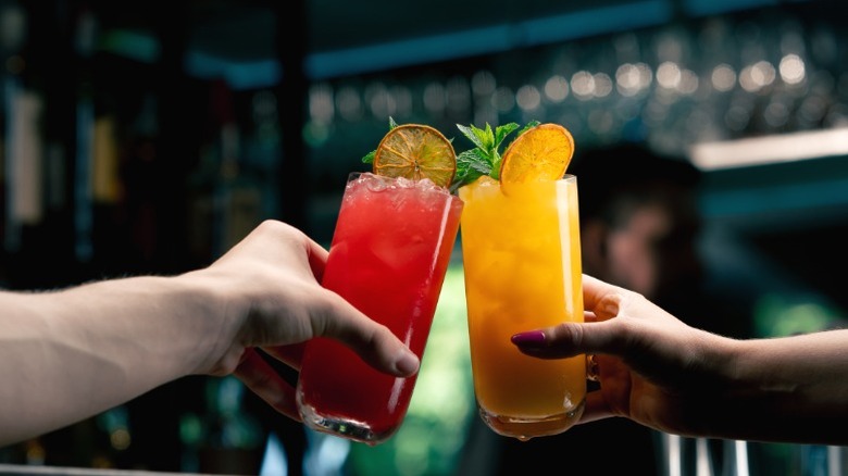 Two fruity cocktails being clinked together at a bar.