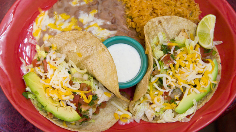 Tacos in a red bowl with a pot of sour cream