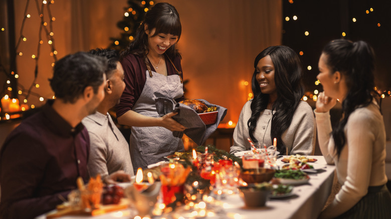 A person at a dinner party serving meat to a table of guests