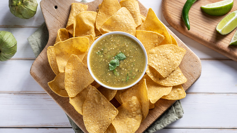 A bowl of green salsa with tortilla chips and fresh vegetables