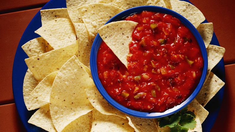 A bowl of red salsa with tortilla chips on a blue plate