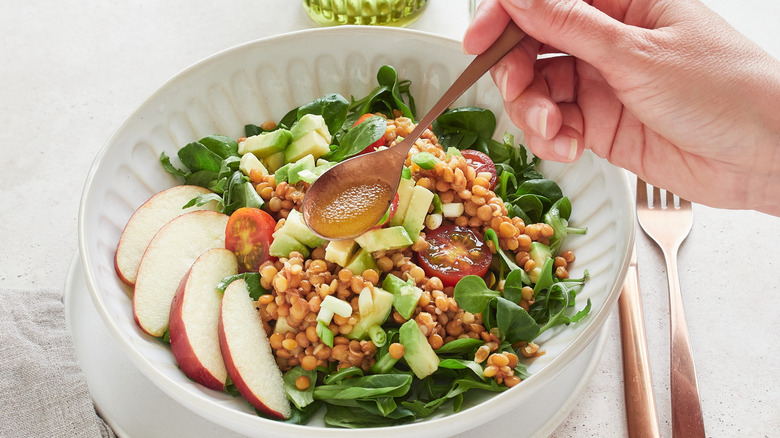 Person's hand holding a spoon with vinaigrette dressing over a bowl of salad