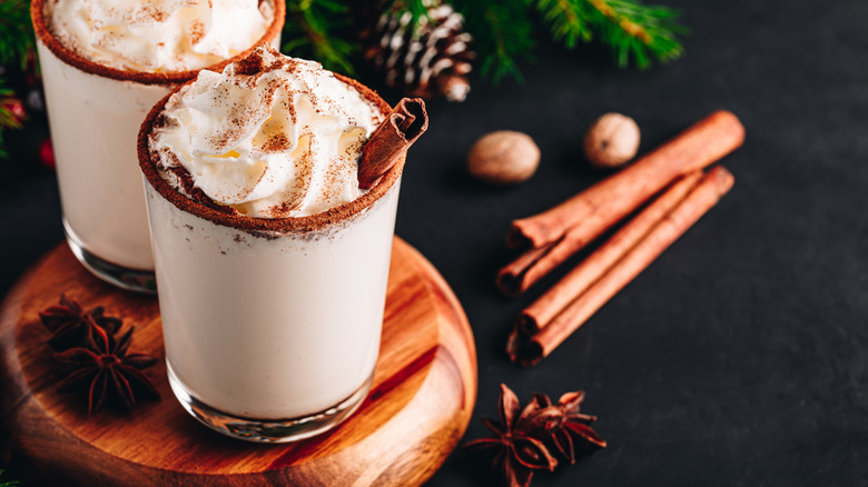 Eggnog with whipped cream and cinnamon sticks on a circular wooden surface