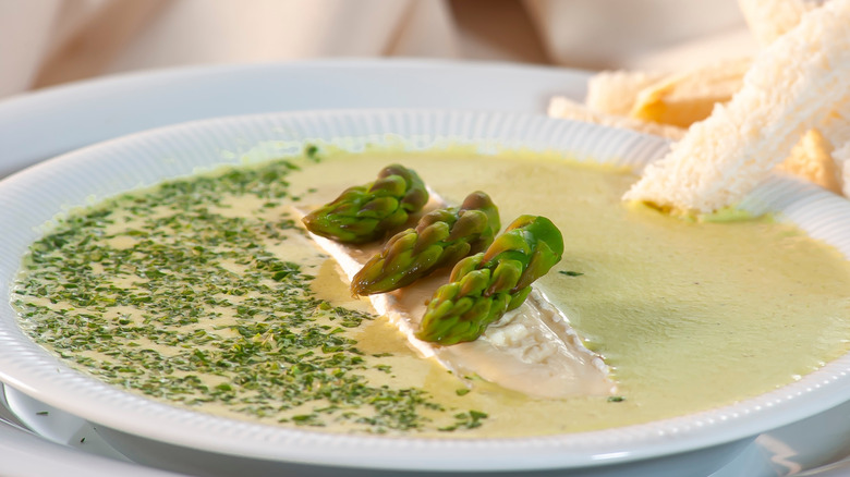 A bowl of creamy asparagus soup with an asparagus tip garnish