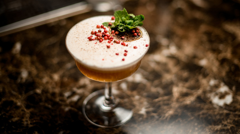 A cocktail in a coupe glass with Sichuan peppercorns on top