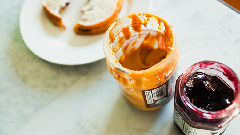 Open jars of peanut butter and jelly next to a sandwich