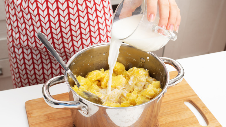 a woman adding milk to cooked potatoes