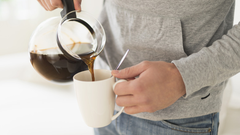 A person pouring coffee from a pot into a mug