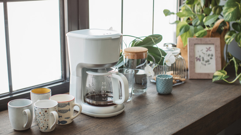 A white coffee maker on a wooden counter with mugs