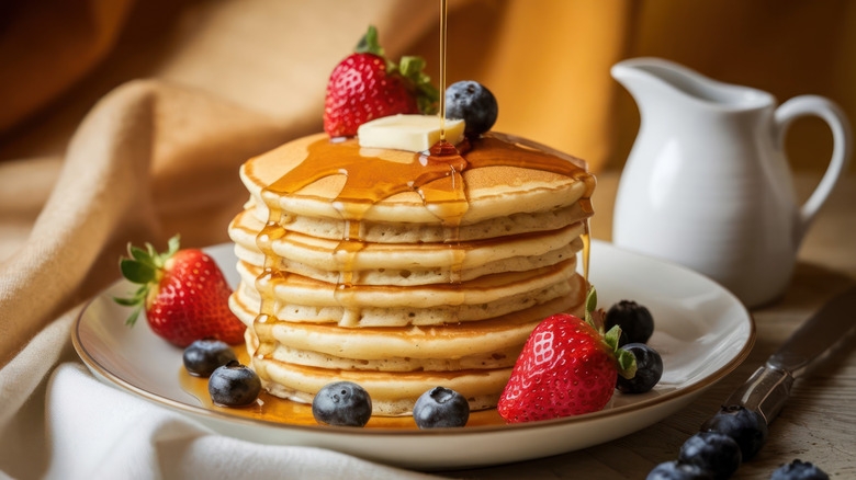 Stack of pancakes with butter, maple syrup, and berries