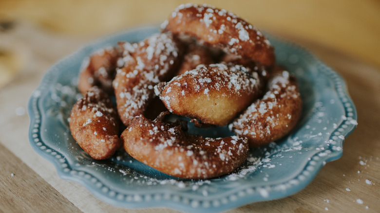 Apple fritters dusted with powered sugar on a teal plate sitting on a wooden surface