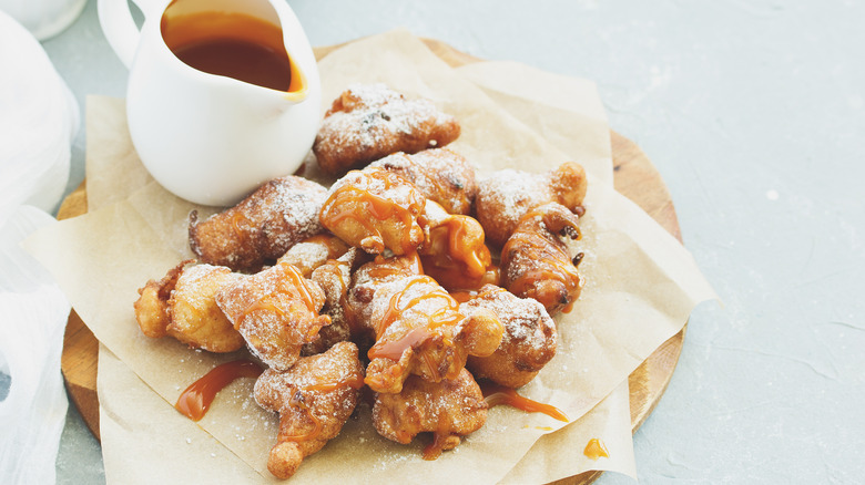 A plate of apple fritters covered in powdered sugar and drizzled with caramel sauce