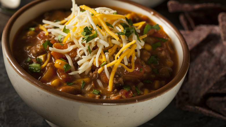 A white and brown bowl filled with chili with shredded cheese on top of it.